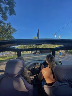 two women sitting in the back of a car looking at something on the road behind them