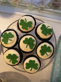 cupcakes decorated with green shamrock leaves on top of a cake plate in front of a window