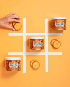 three cans of tea and four cookies on an orange surface with white squares in the middle