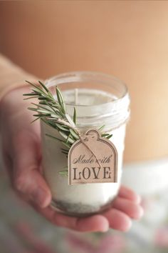 a person holding a jar filled with white liquid and rosemary sprig on top