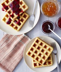 three waffles on plates with jam and jelly