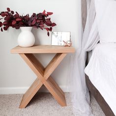 a small wooden table with a vase on it next to a bed and a white curtain