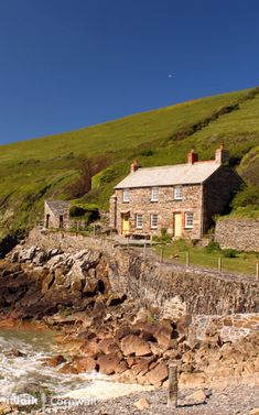 an old stone house sitting on top of a hill next to the ocean with waves crashing in front of it