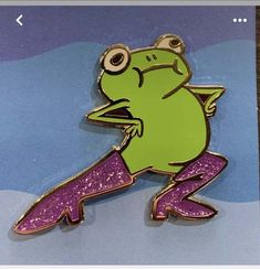 a green frog sitting on top of a purple and pink glittered object with eyes wide open