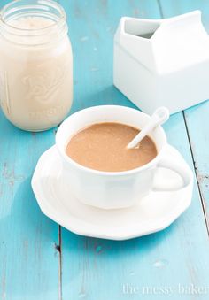 a cup of hot chocolate next to a jar of milk on a blue wooden table