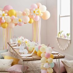 a table topped with lots of balloons in front of a window filled with pink, yellow and white balloons