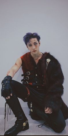 a young man dressed in punk clothing sitting on the ground with his hand on his knee