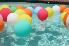 many balloons floating in the water next to a swimming pool