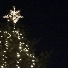 a lighted christmas tree in the dark with a cross on it's top at night