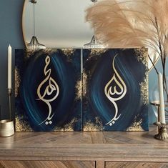 two paintings with arabic calligraphy on them sitting on a table next to a mirror