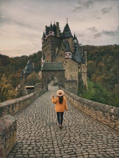 a woman walking across a stone bridge with a castle in the background on a cloudy day