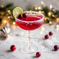 a red cocktail garnished with cranberries and lime