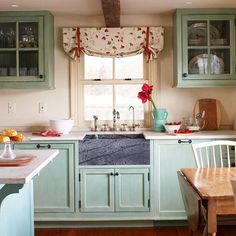 a kitchen with green cabinets and white counter tops, wooden flooring and a window above the sink