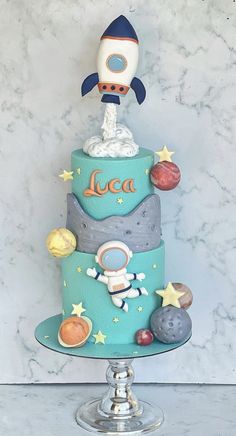 a three tiered cake with an astronaut on top and planets around the edges, sitting on a pedestal