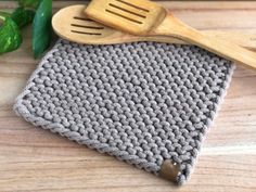 a crocheted dishcloth and wooden utensils are on a table next to green leaves