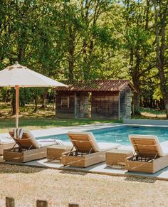 lounge chairs and an umbrella near a pool in the sun with trees behind it,