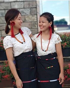 two young women standing next to each other in front of some bushes and flowers with beads on their necklaces