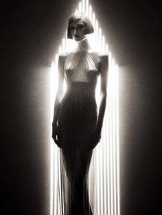 a black and white photo of a woman in a long dress with lights behind her