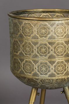 an ornately designed metal bowl on stand with gold colored handles and legs, set against a gray background