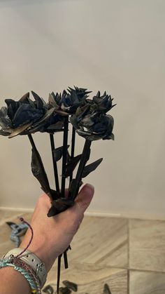 a person holding up some black flowers in their hand on the tile floor next to a wall