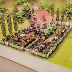 a miniature model of a house surrounded by trees and plants in the foreground is a garden