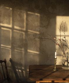 a wooden table topped with a vase filled with flowers next to a candle and a window