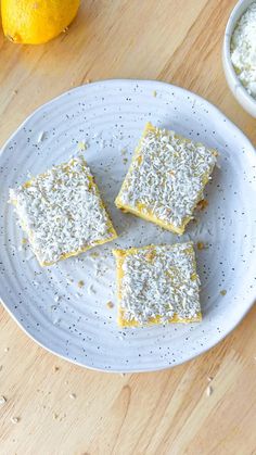 four squares of lemon cake on a white plate next to two bowls of cream cheese