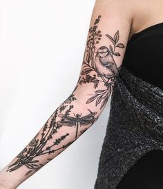 a woman's arm with flowers and birds tattooed on the arm, while she is wearing a black dress