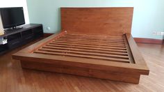 a wooden bed frame in a room with hard wood flooring and a flat screen tv mounted on the wall