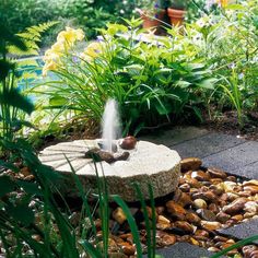 a small fountain in the middle of a garden with rocks and stones around it, spewing water