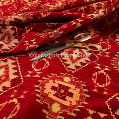 a pair of scissors sitting on top of a red and gold patterned fabric with an intricate design