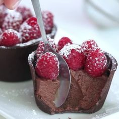 a chocolate dessert with raspberries and powdered sugar on top is being cut