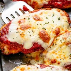 two pieces of chicken parmesan sitting on top of a pan with a fork