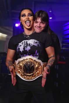 two women standing next to each other with tattoos on their arms and holding wrestling belts