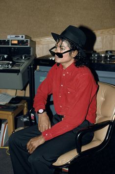 a man in a red shirt and black hat sitting in front of a recording equipment