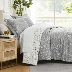 a bed with grey and white comforter next to a window