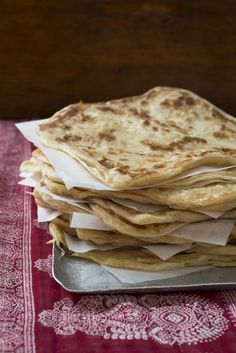 a stack of flatbreads sitting on top of a metal tray next to a red table cloth