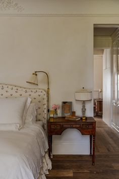 a white bed sitting next to a wooden table with lamps on it's sides