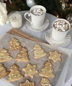 cookies and marshmallows are arranged on a cookie sheet next to two mugs of hot chocolate