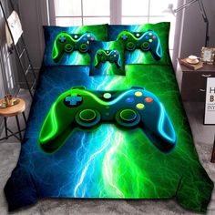 a green and blue bed set with two video game controllers on the cover, in front of a window