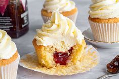 several cupcakes with white frosting and jelly on them next to a bottle of booze