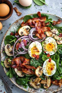 a plate filled with spinach salad topped with hard boiled eggs and sliced mushrooms next to an egg shell