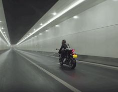 a man riding a motorcycle down a tunnel in the middle of road with lights on