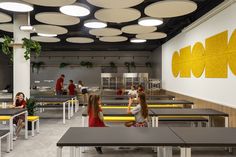 people sitting at tables in a cafeteria with yellow and white accents on the wall behind them