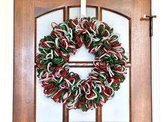 a wreath is hanging on the front door with red, white and green ribbons around it