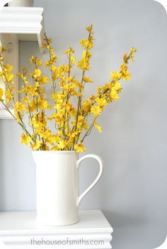 yellow flowers are in a white vase on a shelf