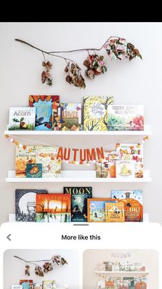 three white shelves filled with books on top of each other and flowers hanging from the ceiling