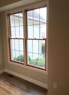 an empty room with two windows and hard wood flooring