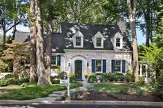 a white house with blue shutters in the front yard and trees on either side