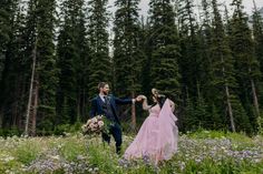 a bride and groom are walking through the woods holding each other's hands with flowers in their hair